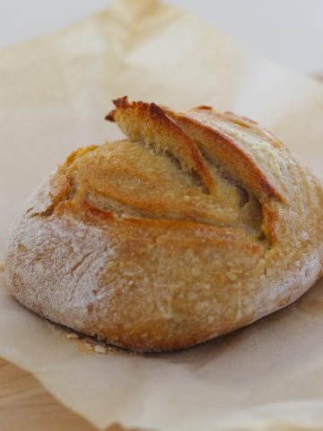 Freshly baked Beginner Sourdough Bread on a parchment paper on a wooden board.